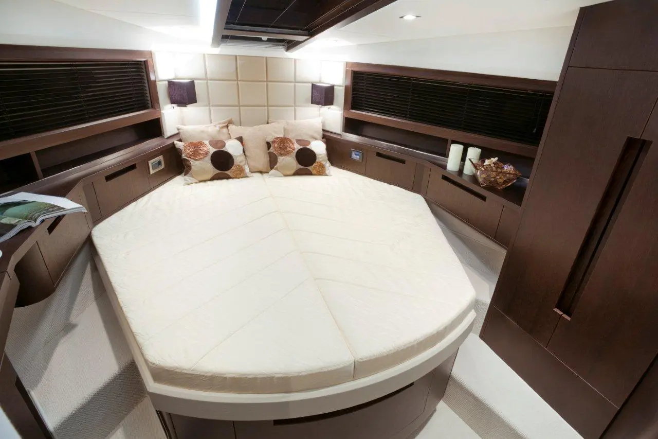 Luxury boat interior featuring a round bed with patterned cushions, ambient lighting, and wooden cabinetry.