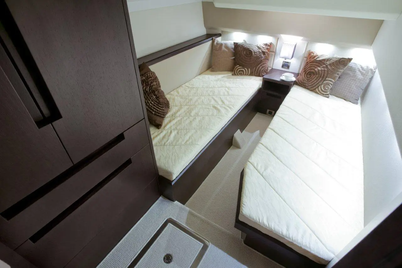 Compact cabin with two single beds, decorative pillows, a bedside table, and dark wood storage units.