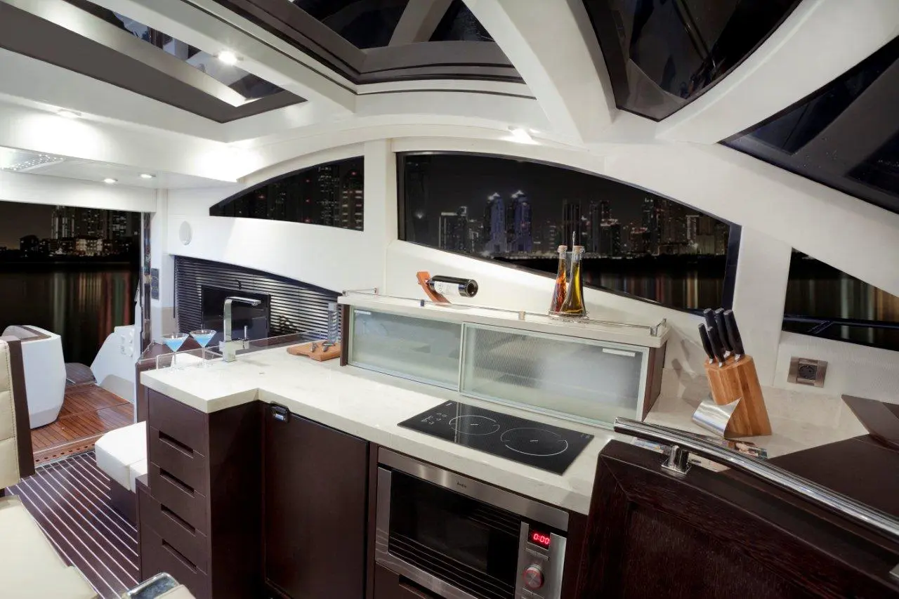 Modern yacht kitchen with sleek cabinets, cooking utensils, and a view of the city skyline through large windows at night.