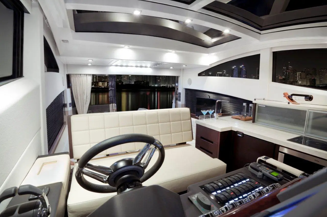Modern yacht interior featuring a steering wheel, seating area, night city skyline views, and a stylish kitchenette.