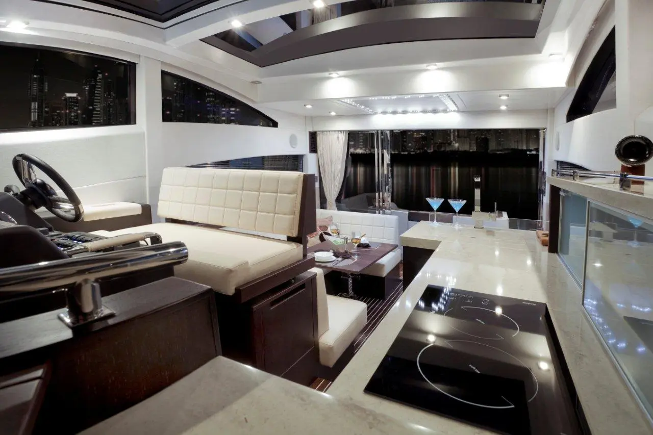 Interior of a luxury yacht with modern kitchen, seating area, and panoramic windows showing city skyline at night.