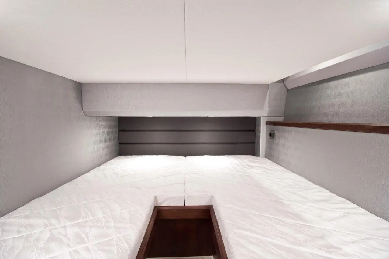 Modern minimalist bedroom featuring two single beds with white mattresses and a wooden storage compartment in the centre.