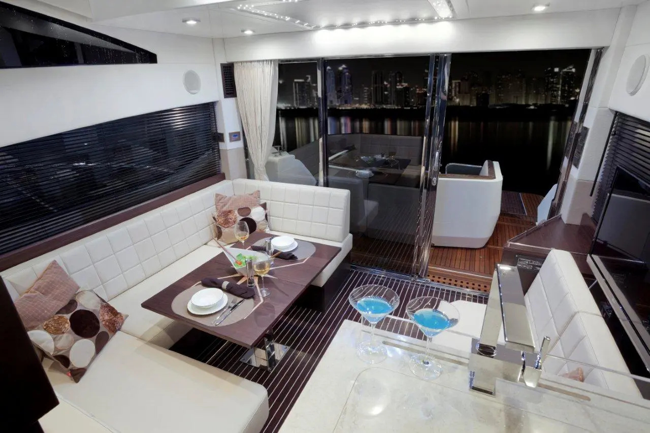 Luxurious yacht interior with plush seating, dining setup, blue cocktails, and city skyline view through large glass doors.