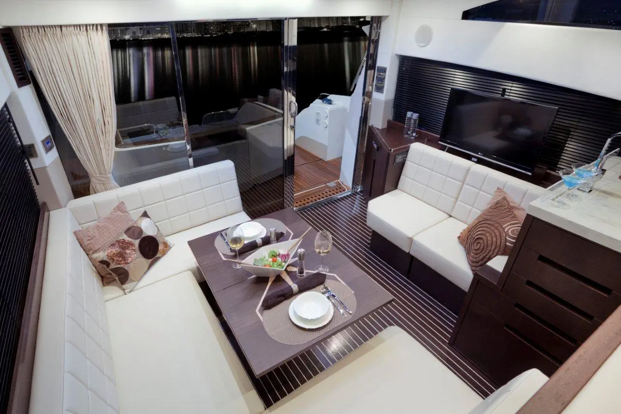 Luxury boat interior featuring a dining area with white sofas, a table set for a meal, and a view of water through glass doors.