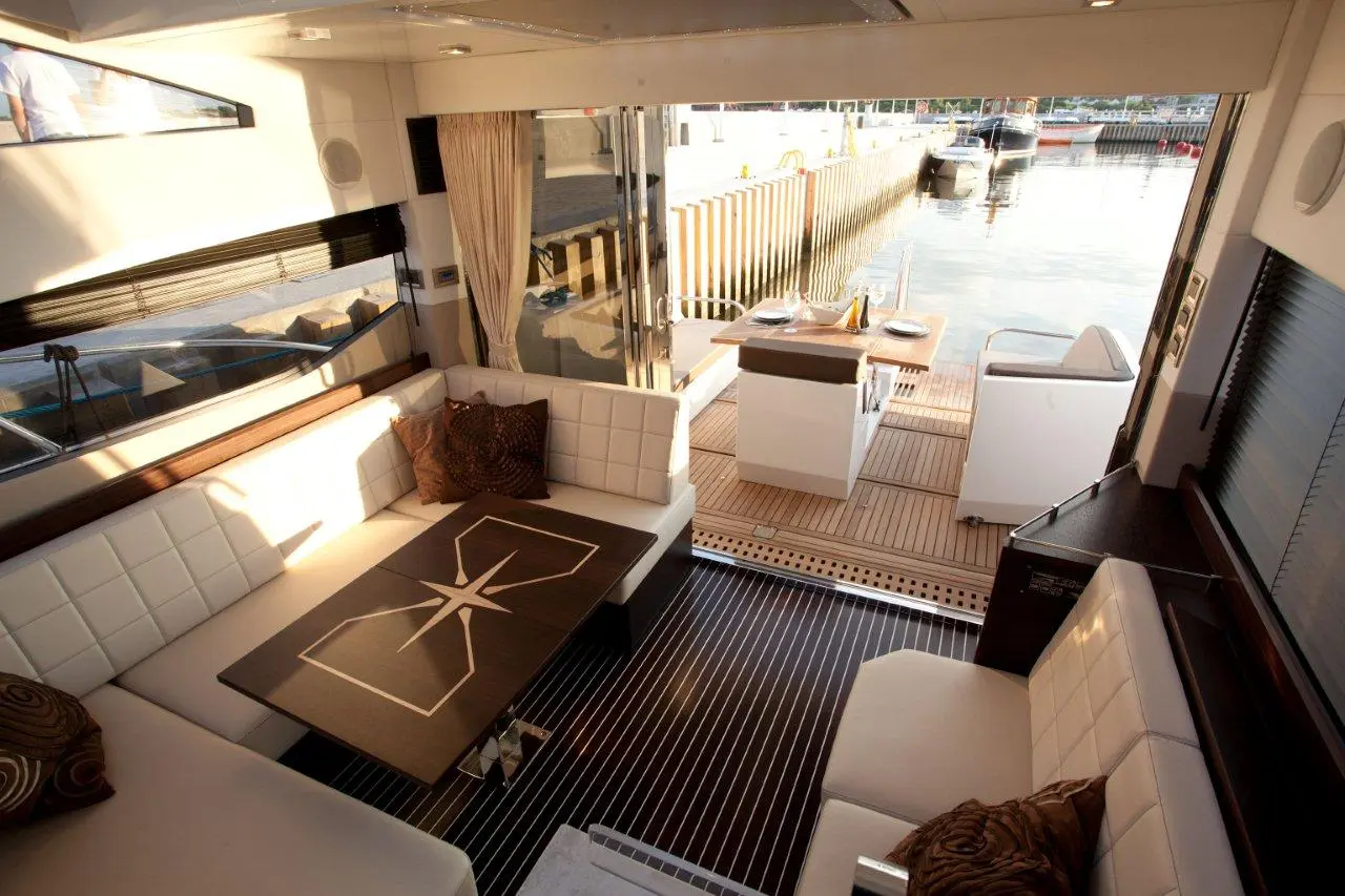 Luxurious yacht interior with white seating, a stylish table, and a view of the marina, promoting boat relaxation and dining.