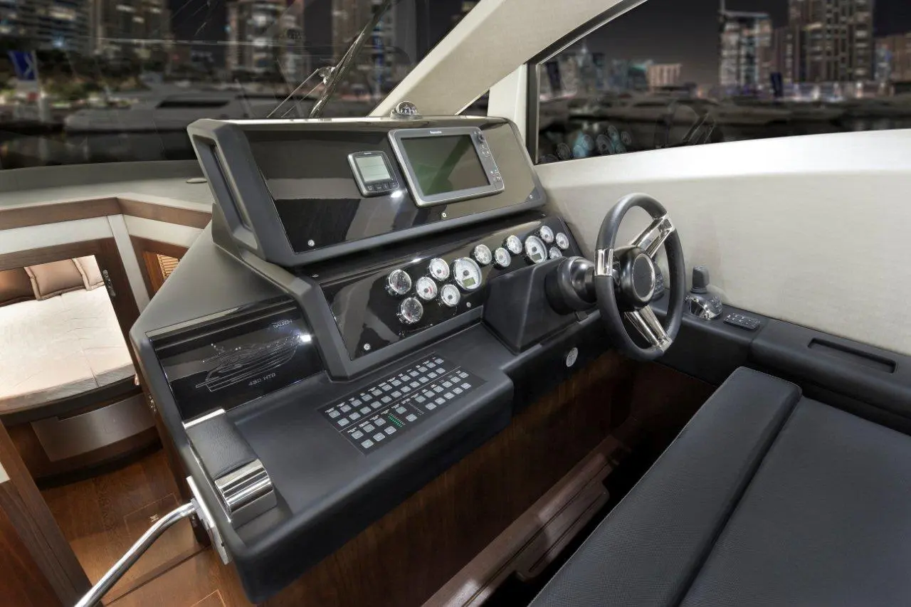 Luxury boat cockpit featuring a steering wheel, control panel, and digital display with a city skyline visible through the window.