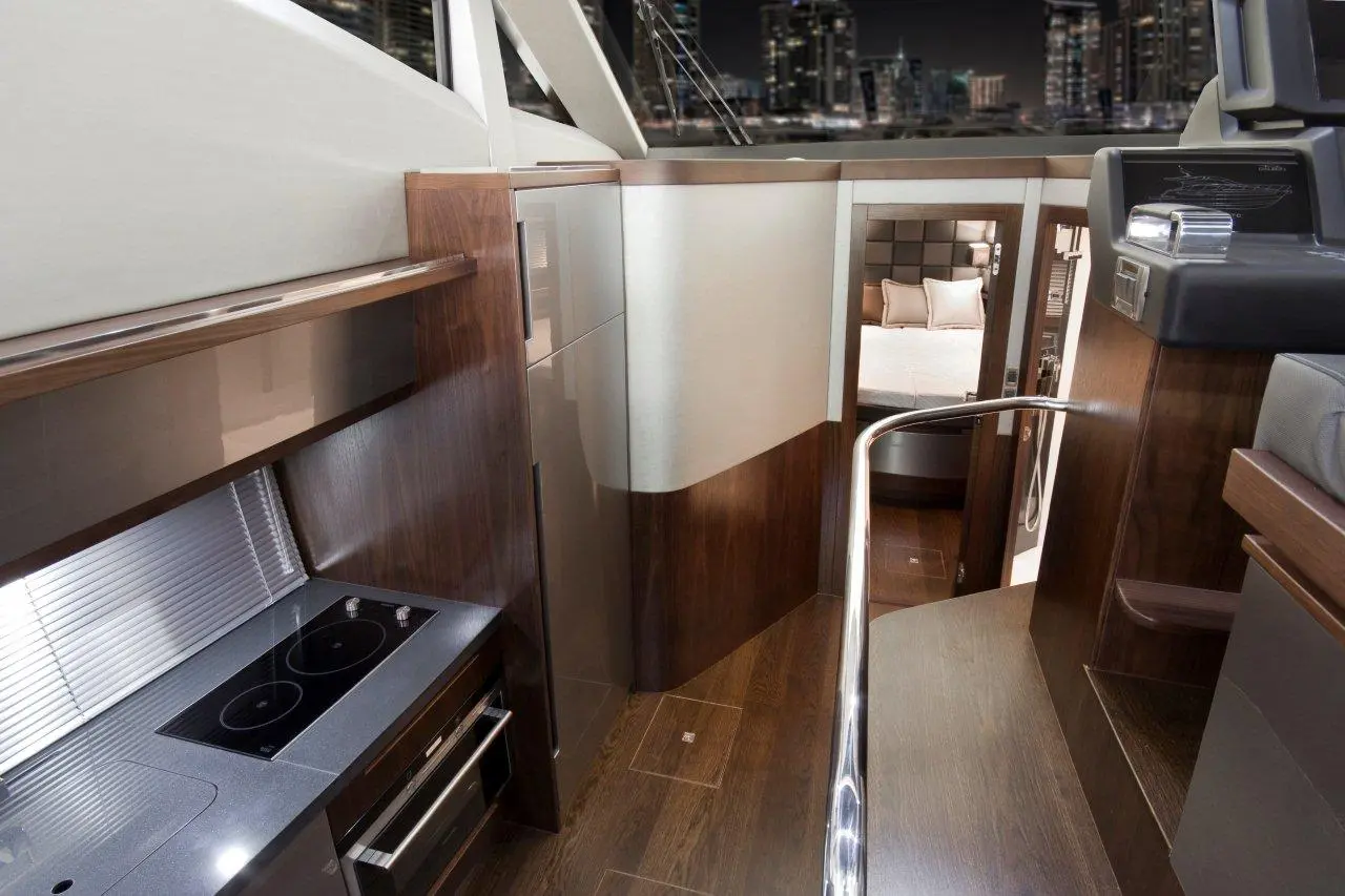 Modern yacht interior featuring a kitchen area with a stovetop, sleek cabinets, and a view of the bedroom space.