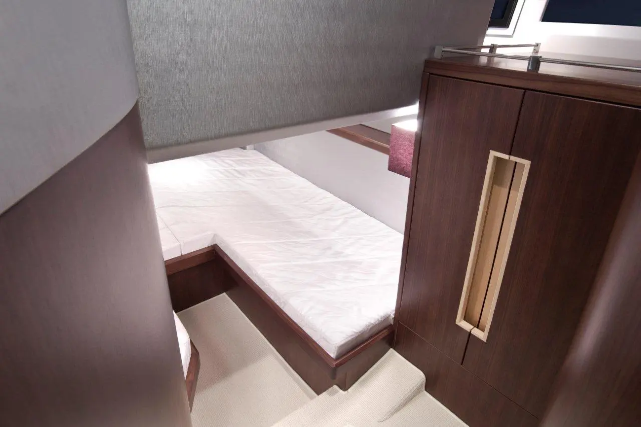 Interior of a modern boat cabin featuring a single bed, wooden furniture, and a grey partition wall.