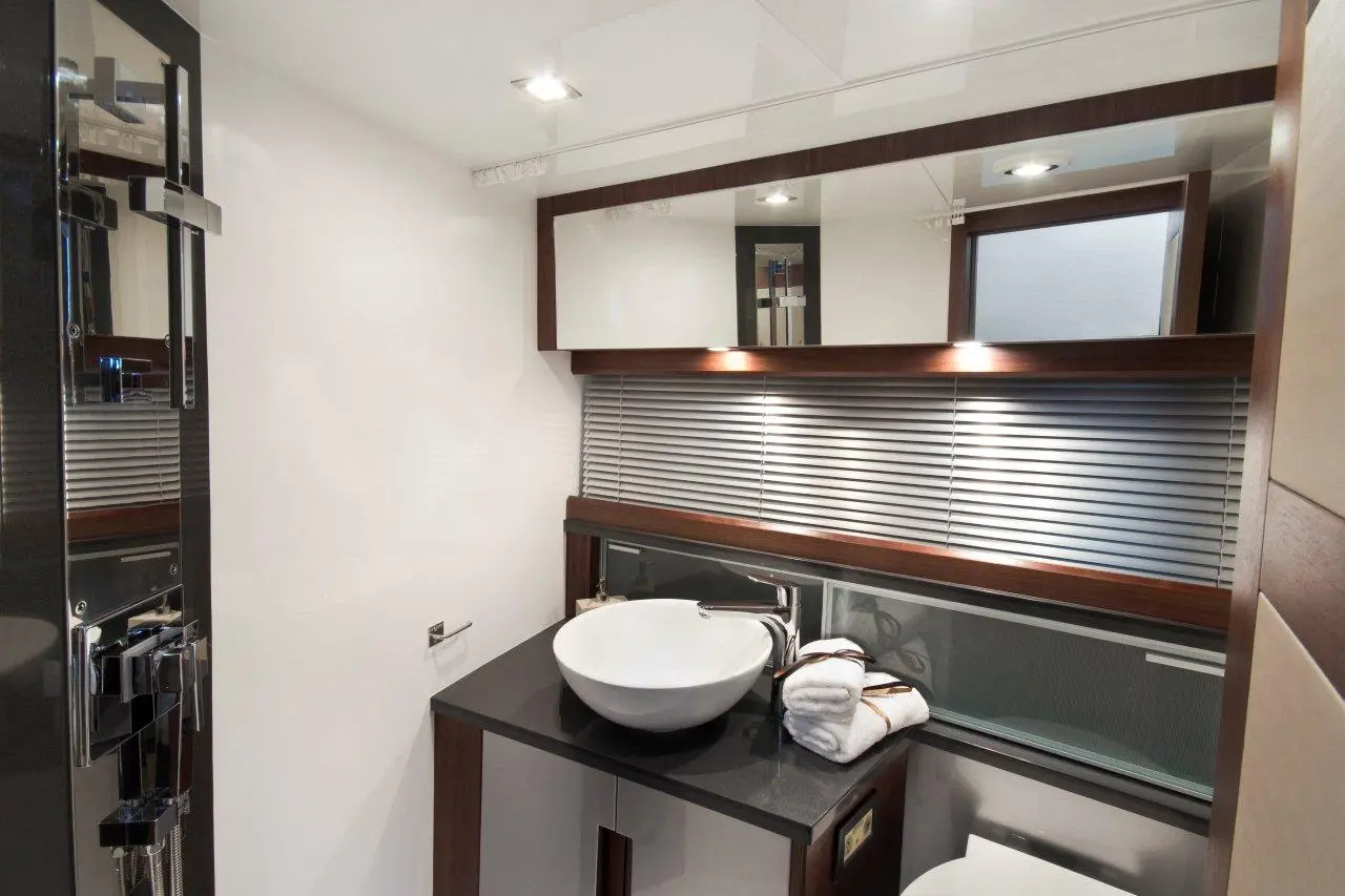 Modern bathroom interior featuring a round basin, wooden cabinetry, towels, and stylish mirror with ambient lighting.