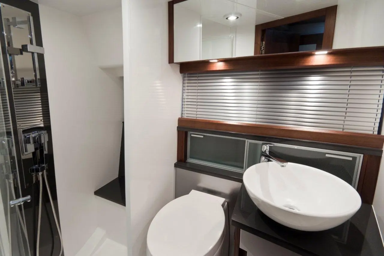 Modern bathroom featuring a shower area, toilet, and a round sink on a black countertop with wooden accents.