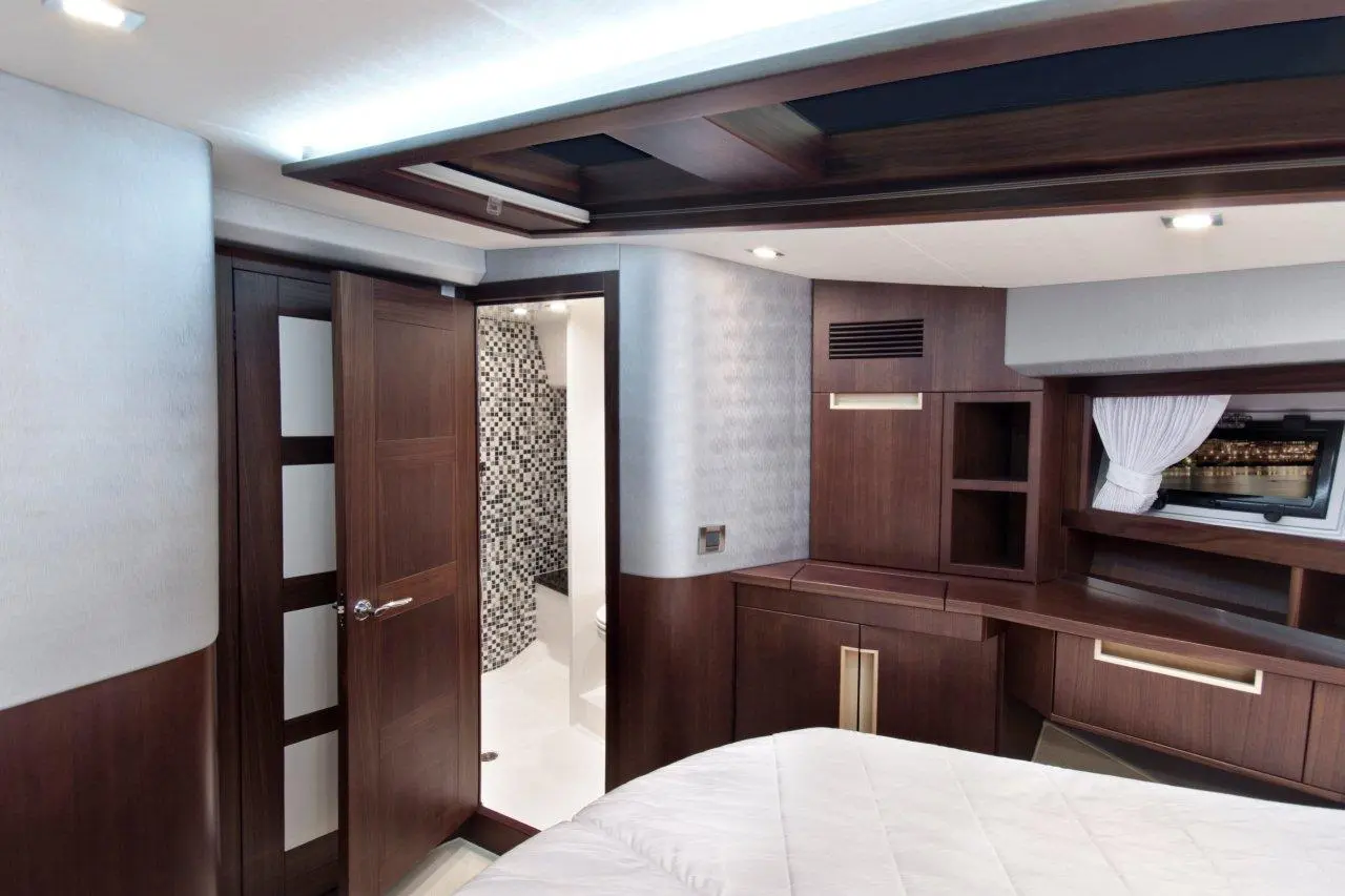 Modern yacht cabin with wooden furnishings, a partially open door, and a bathroom area with tiled walls visible.