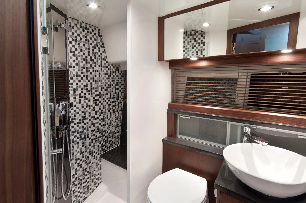 Modern bathroom with black and white mosaic tiles, glass shower, circular sink, and wooden cabinetry. Elegant design.
