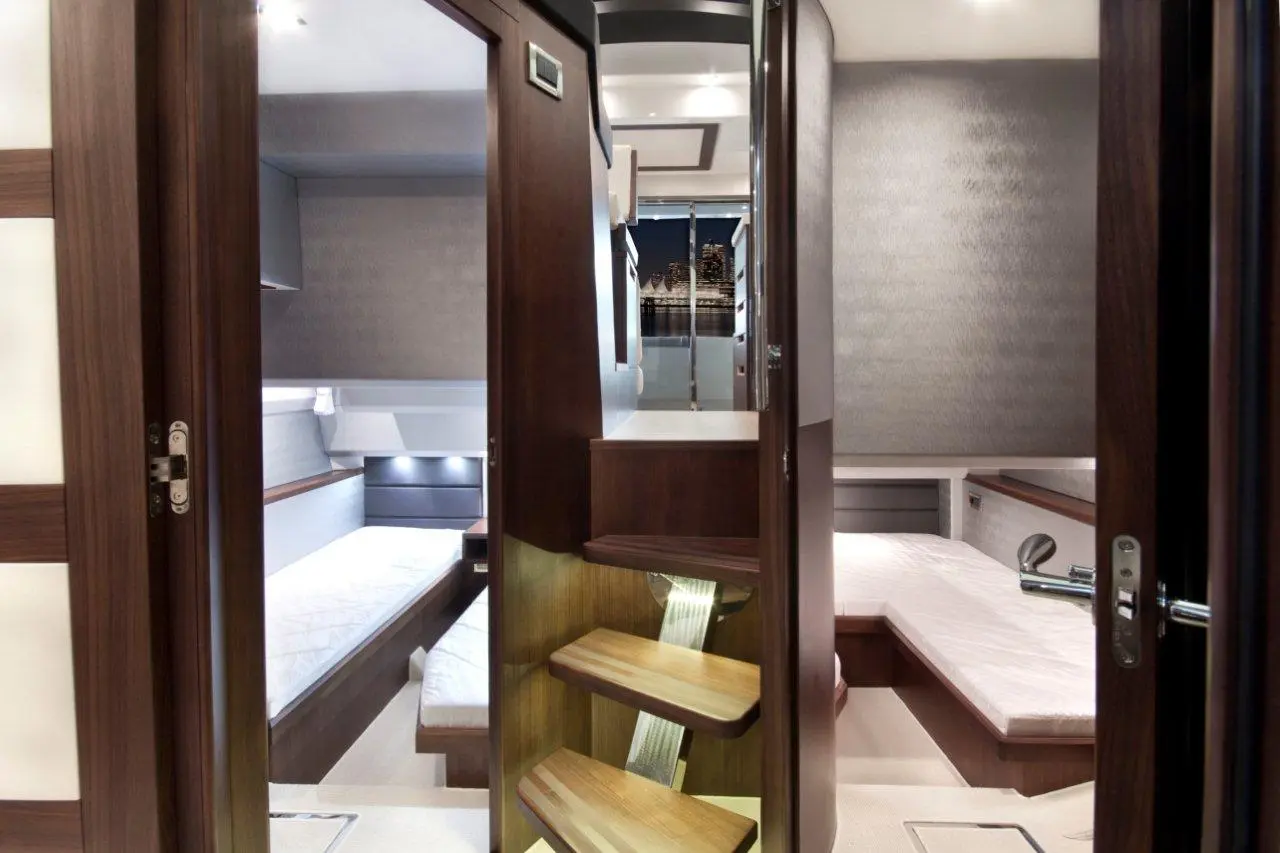 Modern yacht interior featuring wooden stairs, sleeping areas, and a scenic window view of a city skyline at night.