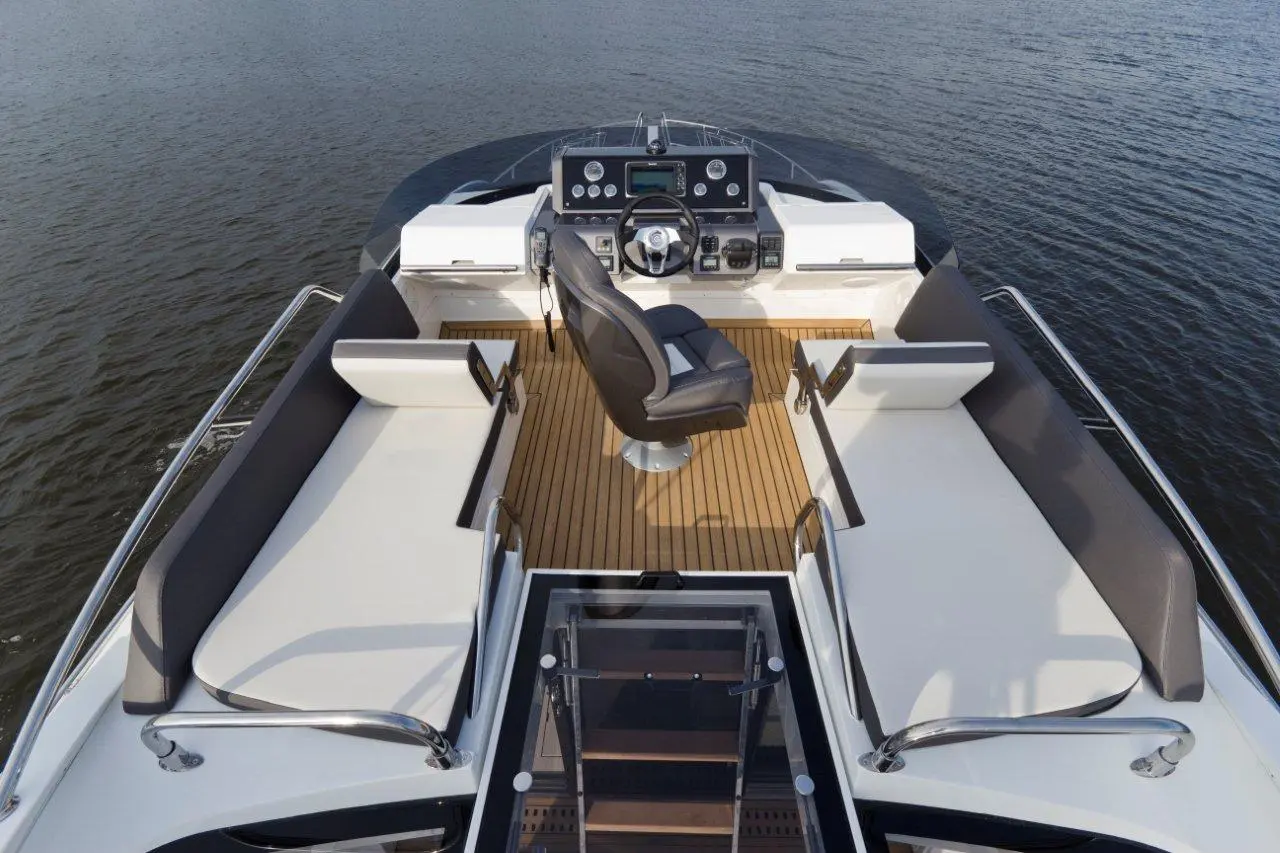 Modern boat cockpit featuring a black captain's chair, seating areas, and navigational controls against a water backdrop.