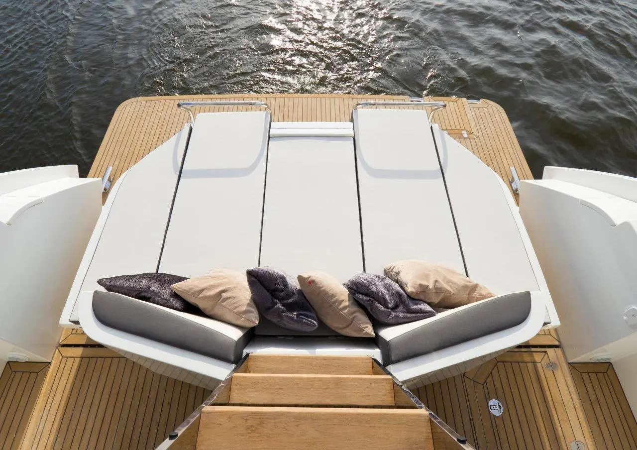 Luxury boat deck featuring sun loungers with cushions, wooden flooring, and water reflecting sunlight. Ideal for relaxation.