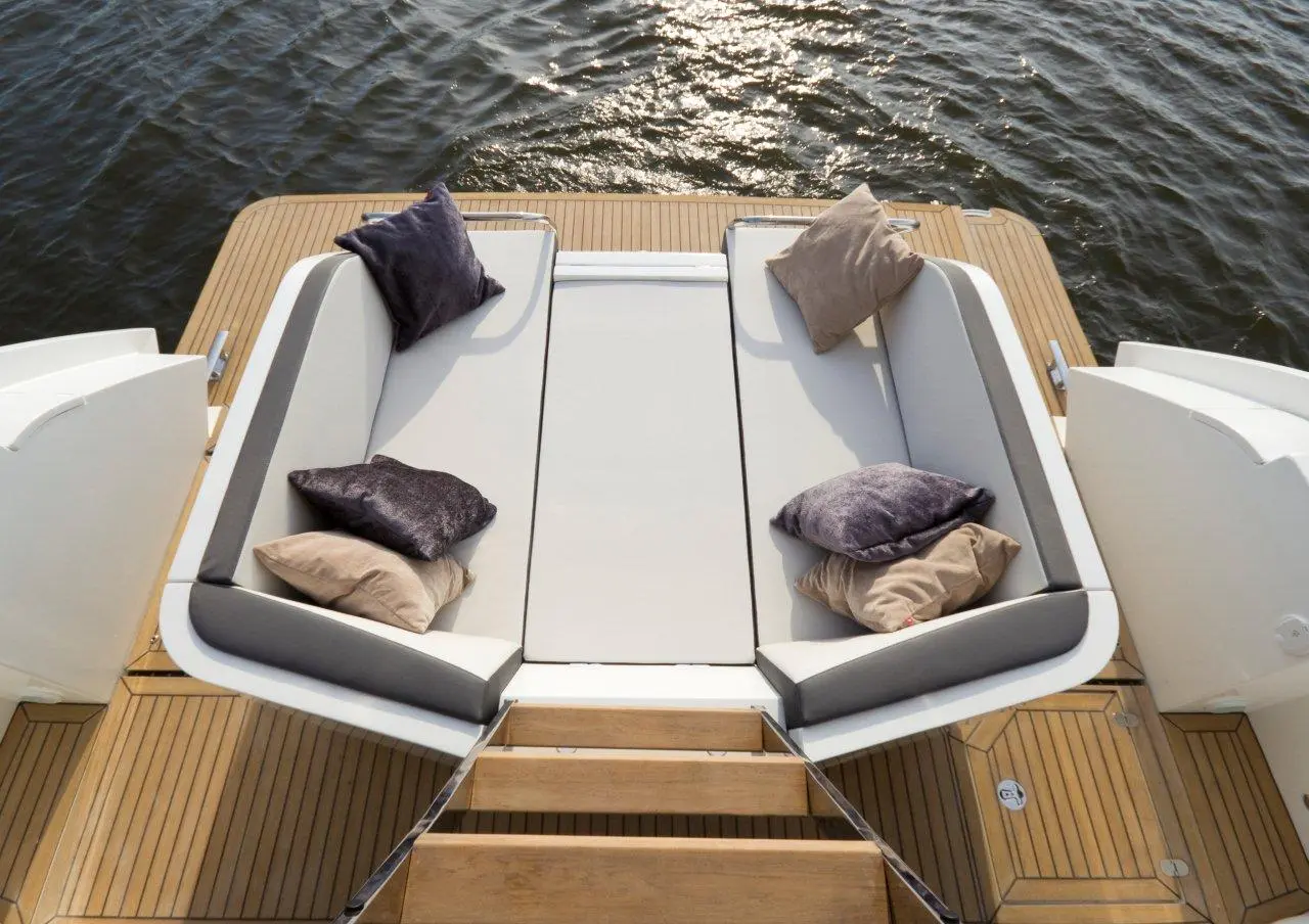 Stylish boat seating area with plush cushions, overlooking shimmering water and wooden decking. Perfect for relaxing outdoors.