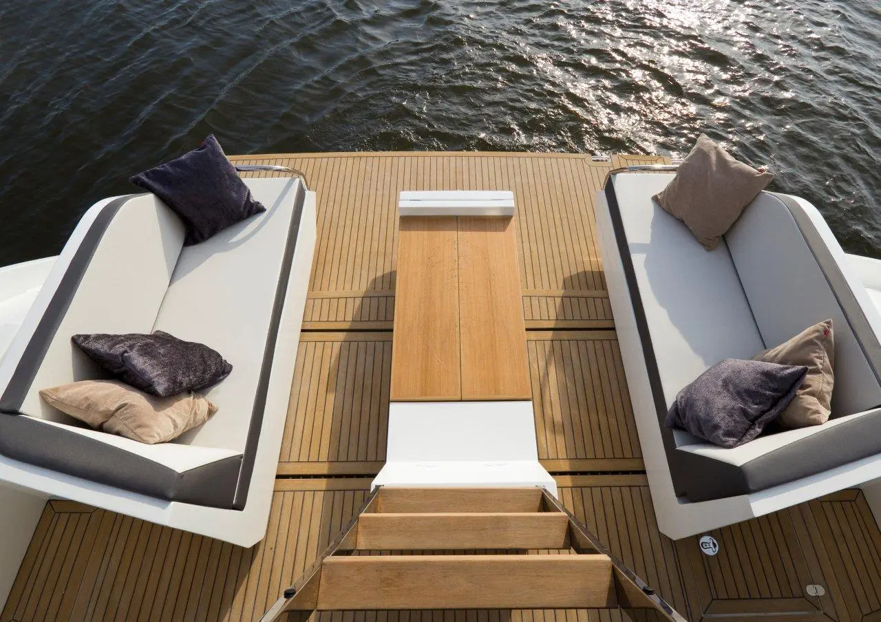 Luxury yacht deck featuring two stylish sofas with cushions, a wooden table, and water reflections in the background.