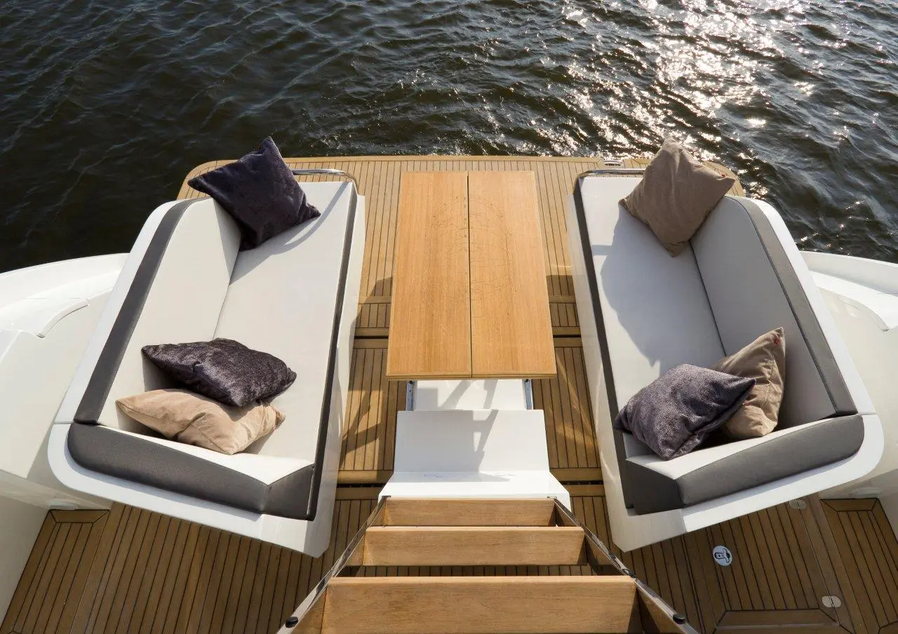 Luxury boat deck featuring two grey sofas with cushions, a wooden table, and steps leading down to the water.