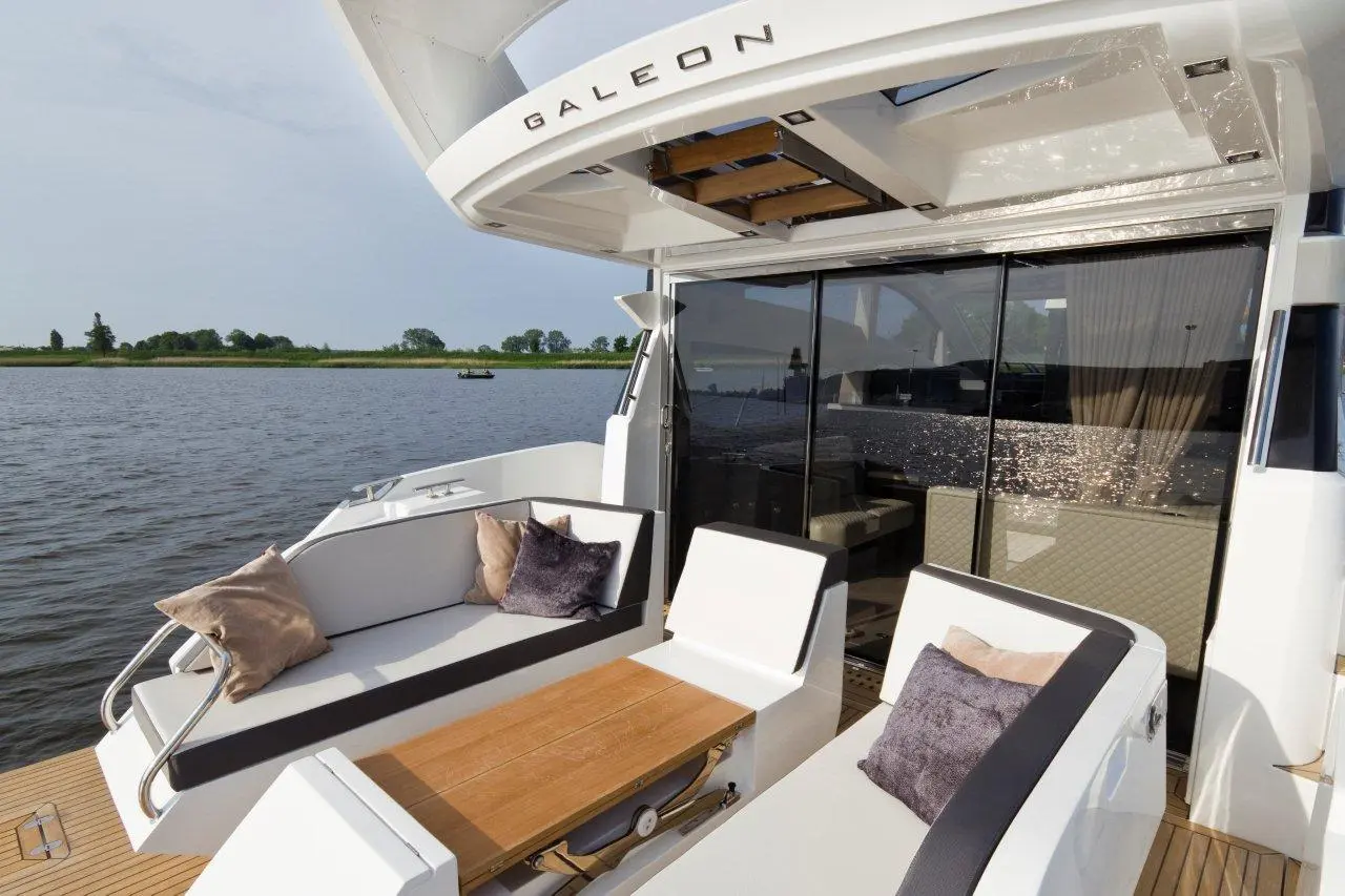 Luxury boat deck featuring plush seating, a wooden table, and panoramic views of the river and greenery beyond.