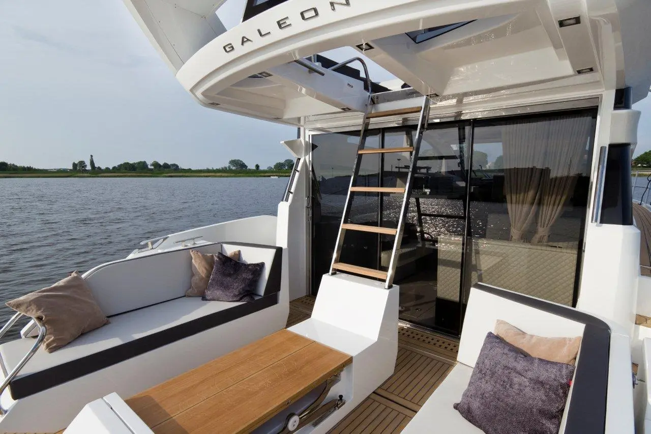 Luxury yacht deck featuring a wooden table, plush seating, and a ladder to the upper deck, with scenic waterfront views.