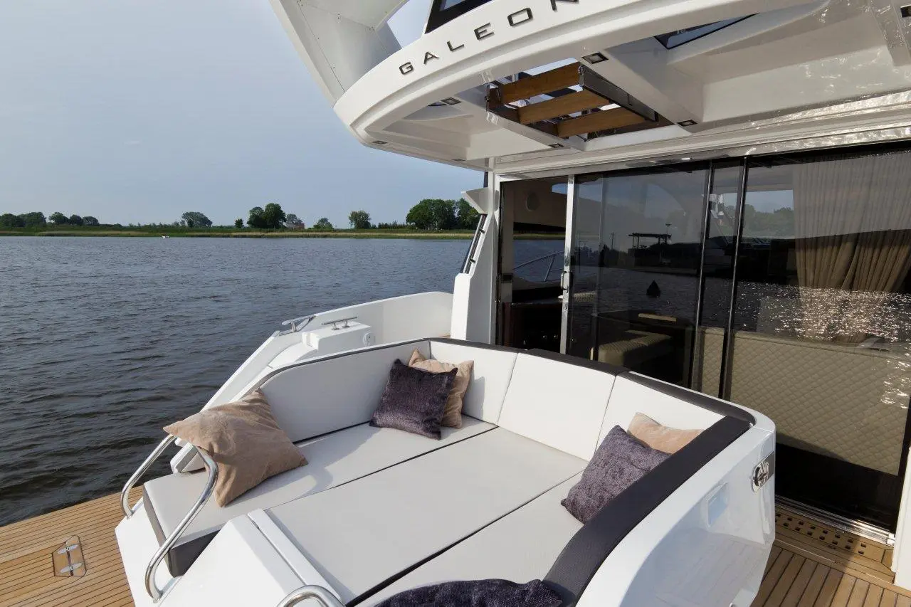 Luxury yacht interior featuring a plush seating area with cushions, overlooking a tranquil waterway and green landscape.