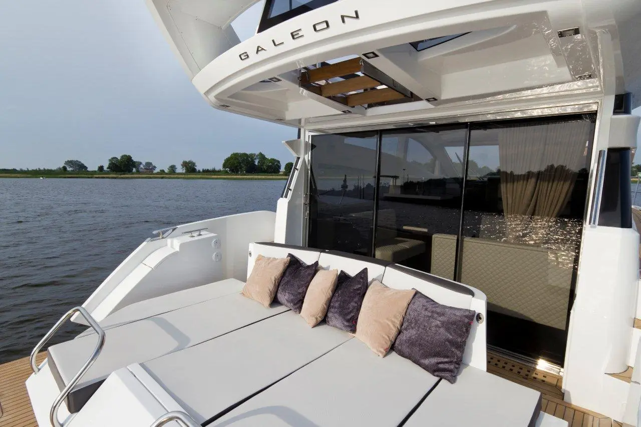 A sleek yacht deck with a cushioned seating area, featuring pillows, overlooking calm waters and greenery in the background.