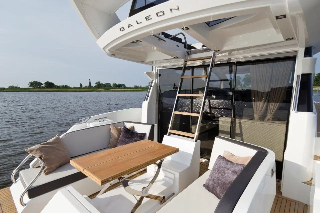 Luxury yacht deck with a wooden table, plush pillows, and a ladder leading to an upper area overlooking the water.