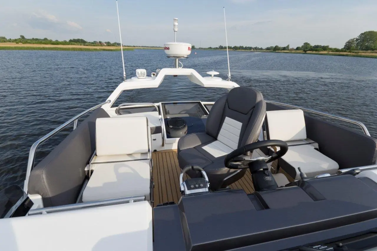View from the helm of a modern boat with grey and white seating, steering wheel, and water in the background.