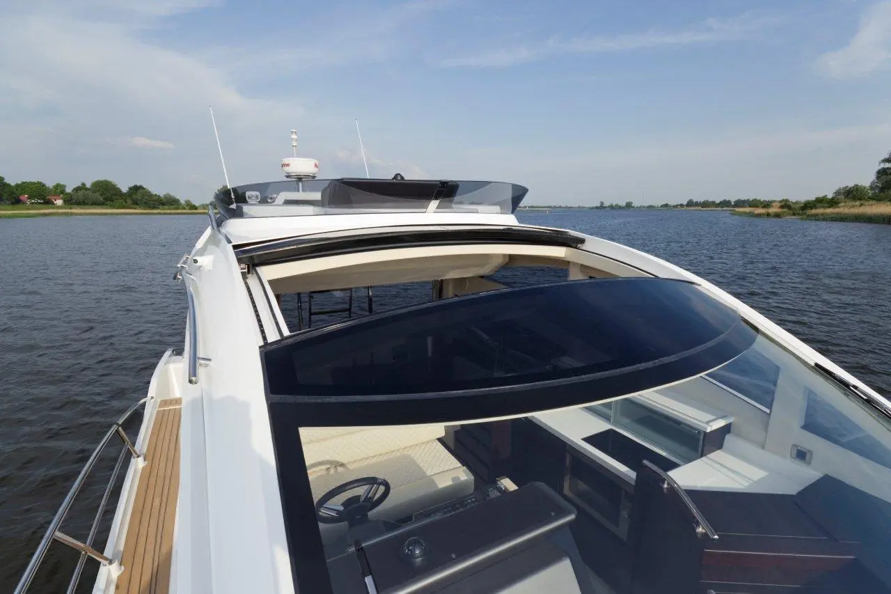 Luxury yacht cockpit view on calm water, with a spacious helm, large windows, and scenic greenery in the background.
