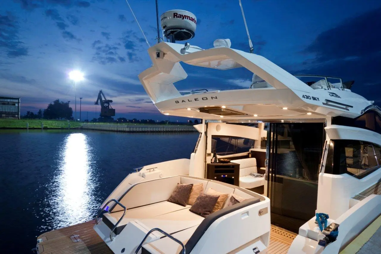 Luxury Galeon 430 SKY yacht at twilight, showcasing a comfortable seating area and illuminated interior against a serene water backdrop.