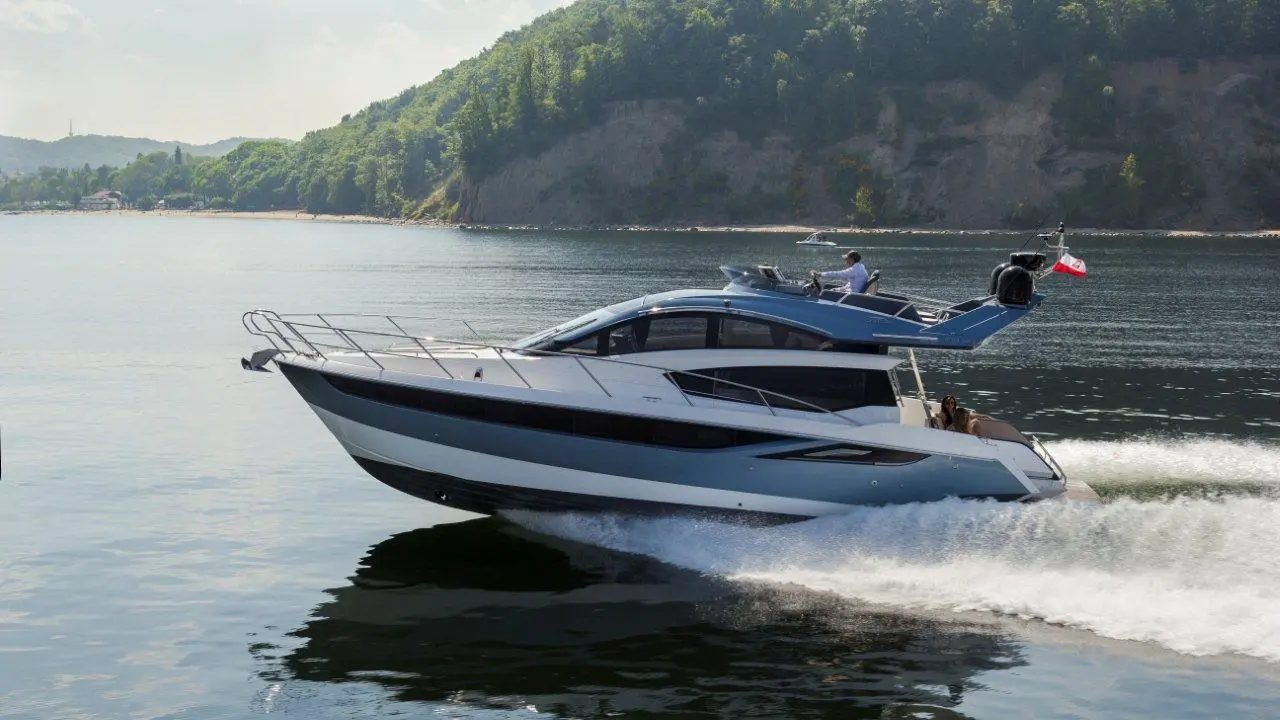 A luxury motorboat speeds across calm water, with green hills in the background and a passenger enjoying the ride.