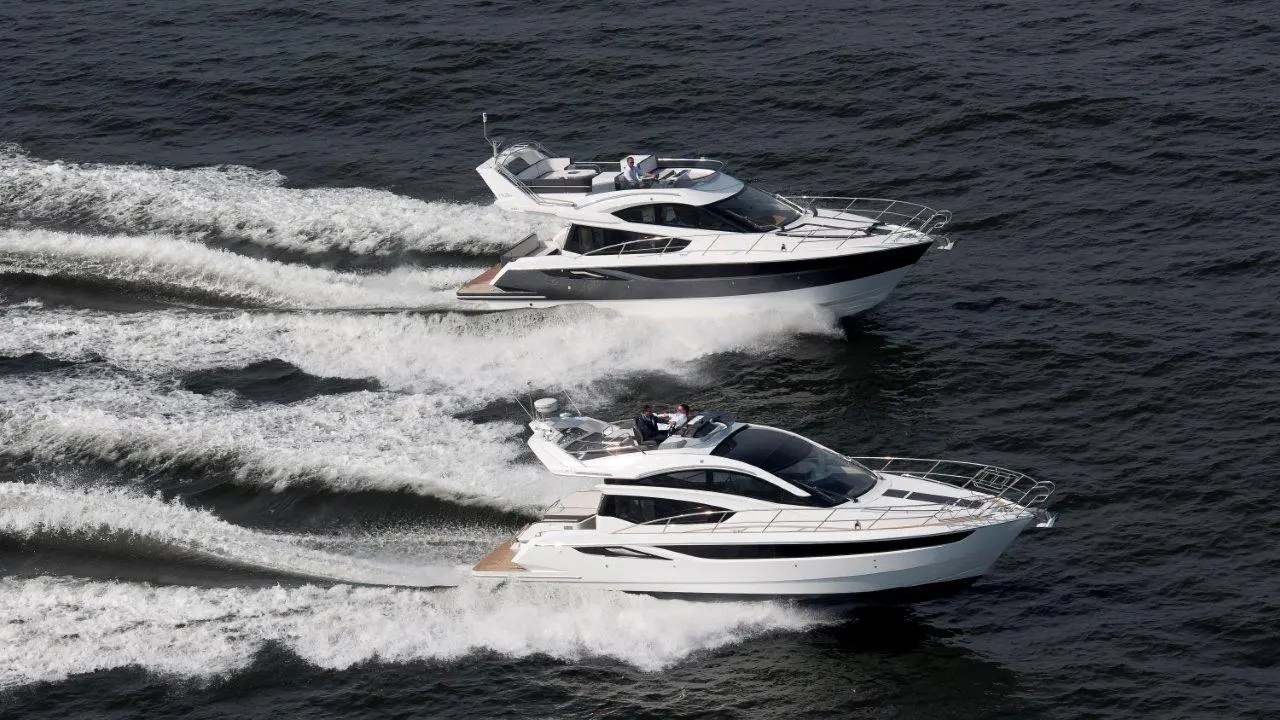 Two luxury motor yachts accelerate over dark water, leaving white spray in their wake under a clear sky.