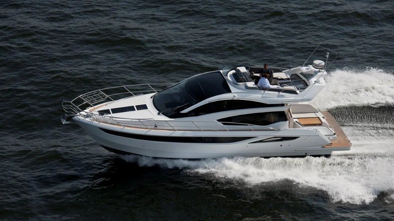 A sleek white yacht navigating through water, with two individuals onboard enjoying a sunny day at sea.