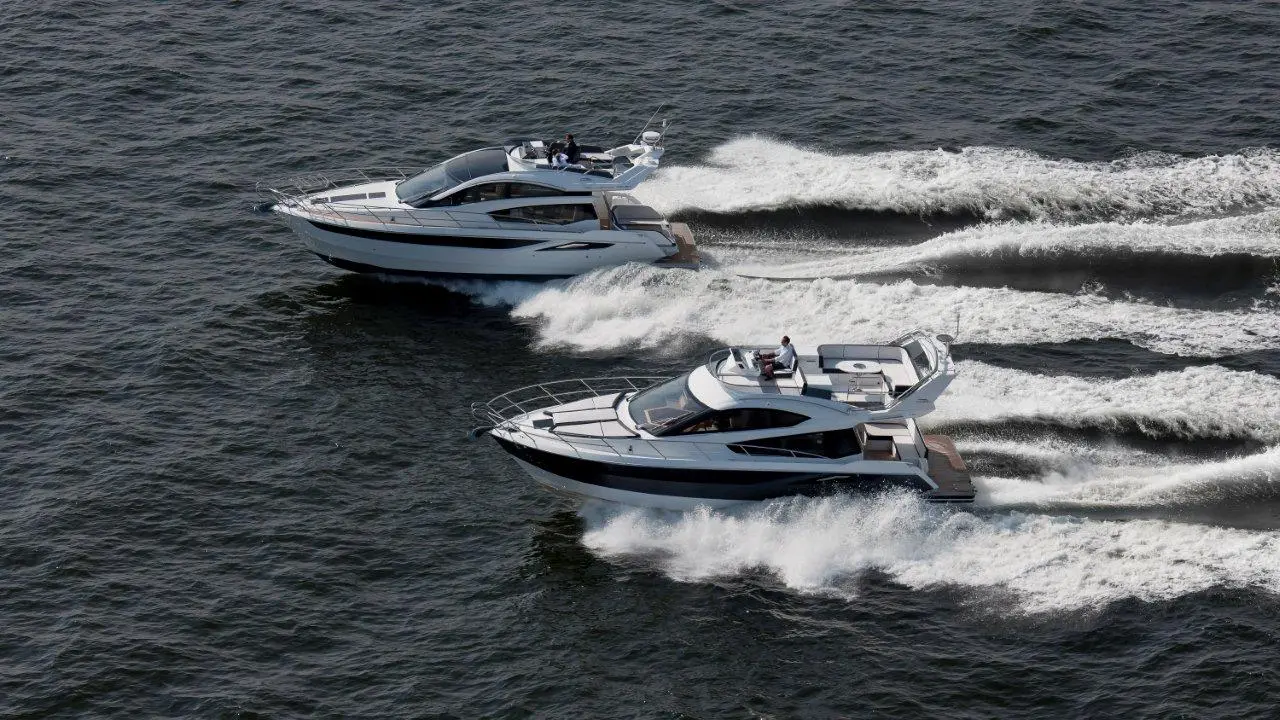 Two luxury motor yachts cruising on calm waters, leaving white wakes behind them in a clear blue sky setting.