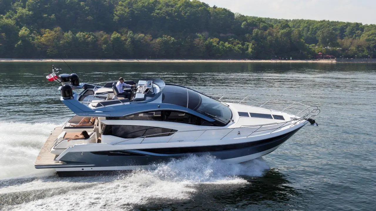 A sleek motor yacht speeds across calm water, with a driver at the helm and guests lounging on deck.