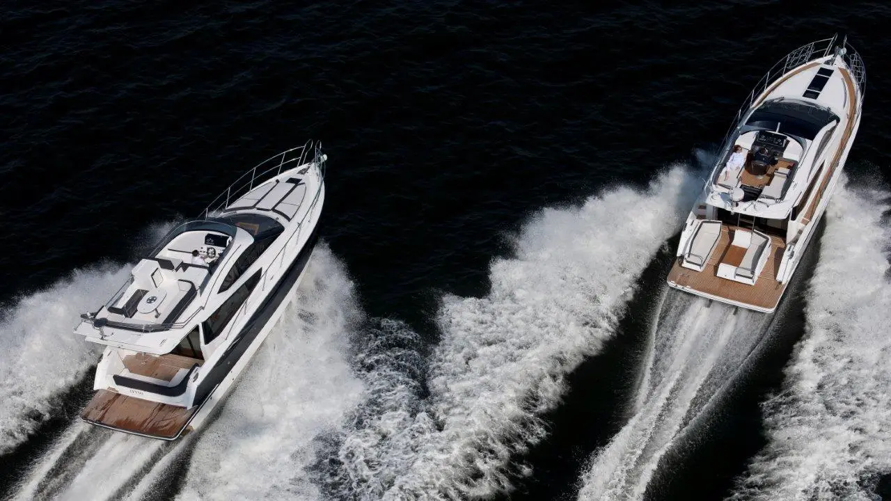 Two luxury motor yachts speed through dark waters, creating white frothy waves behind them.