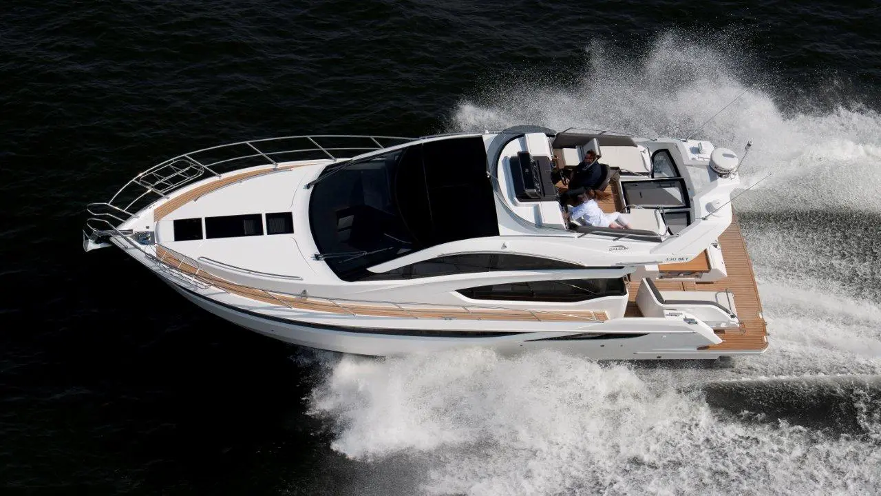A sleek motorboat gliding over water, with two people aboard enjoying the ride on a sunny day.