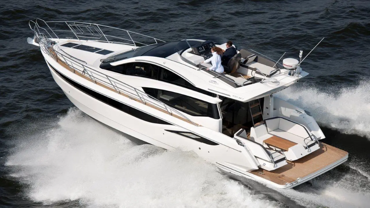 A luxury motorboat cruising through water, with two people at the helm, showcasing sleek design and modern features.