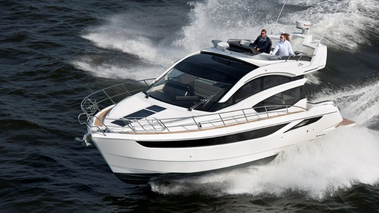 A modern white luxury yacht speeds across water, with two people at the helm, highlighting recreational boating adventures.