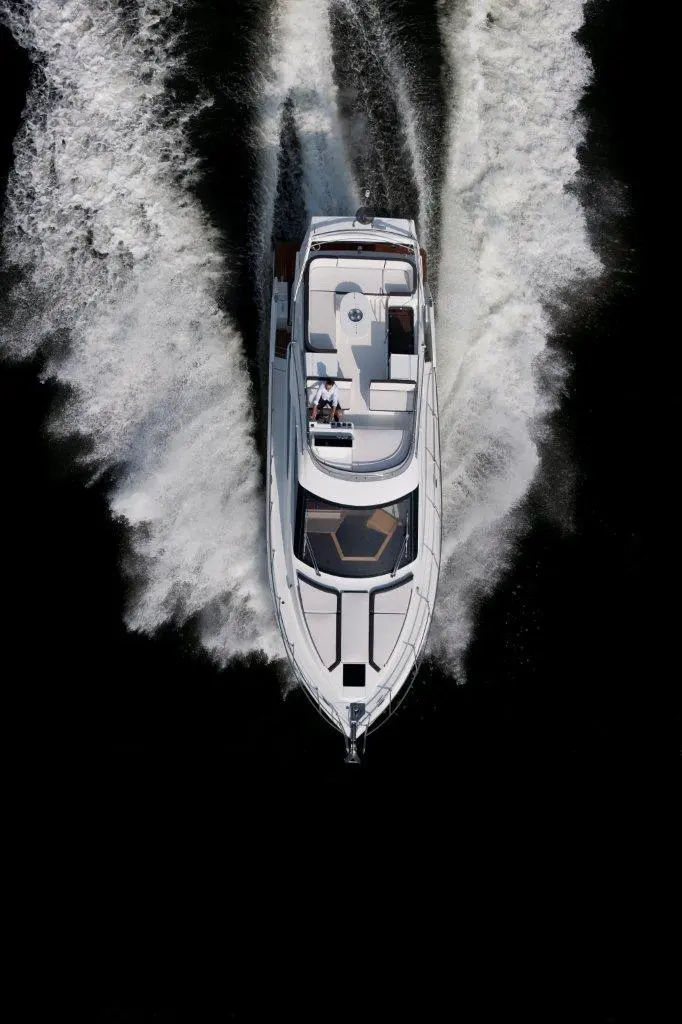White motorboat speeding through dark waters, leaving a frothy trail behind. Luxurious deck visible, showcasing seating area.