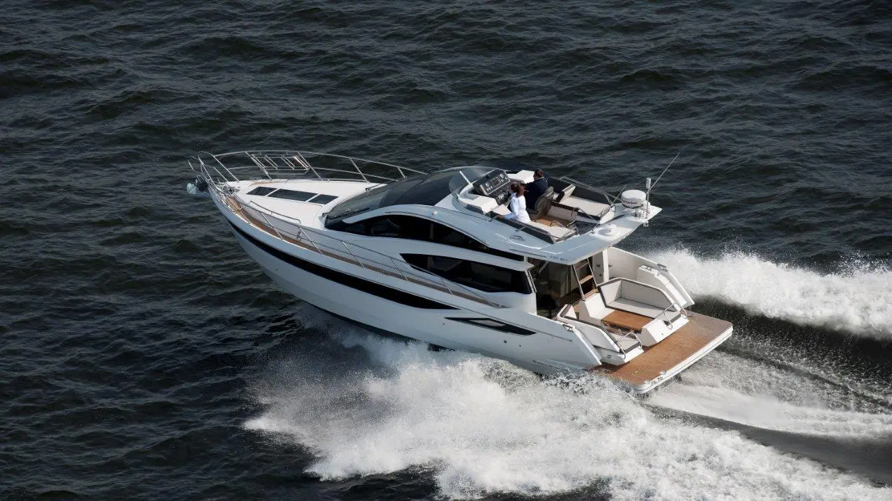 A sleek powerboat cruising on calm waters, with two people on deck enjoying the ride under clear skies.