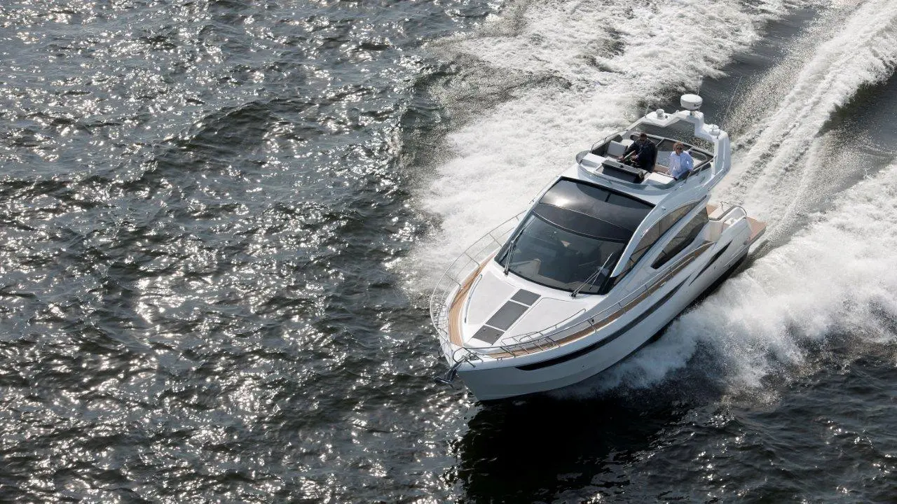 A sleek motorboat speeds through sparkling water, leaving a foamy wake behind while two people enjoy the ride on board.