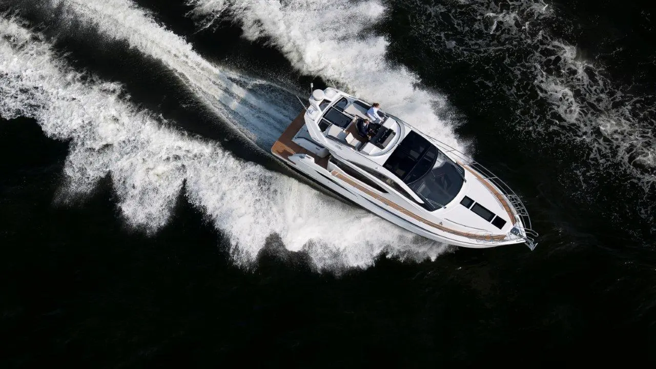 A white motorboat navigates through dark waters, leaving a wake of frothy waves behind it.