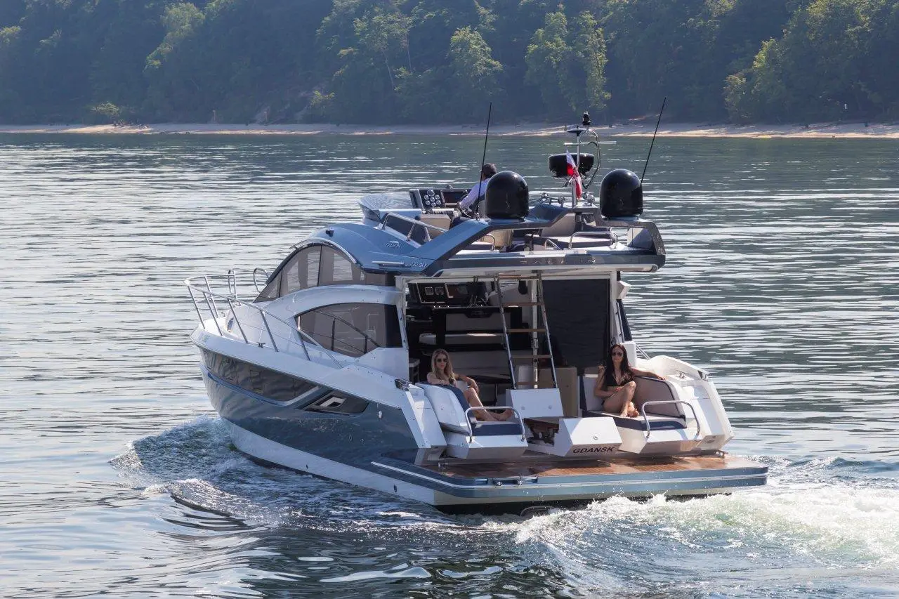 Luxury yacht cruising on calm waters, with two women relaxing on the deck and lush greenery in the background.