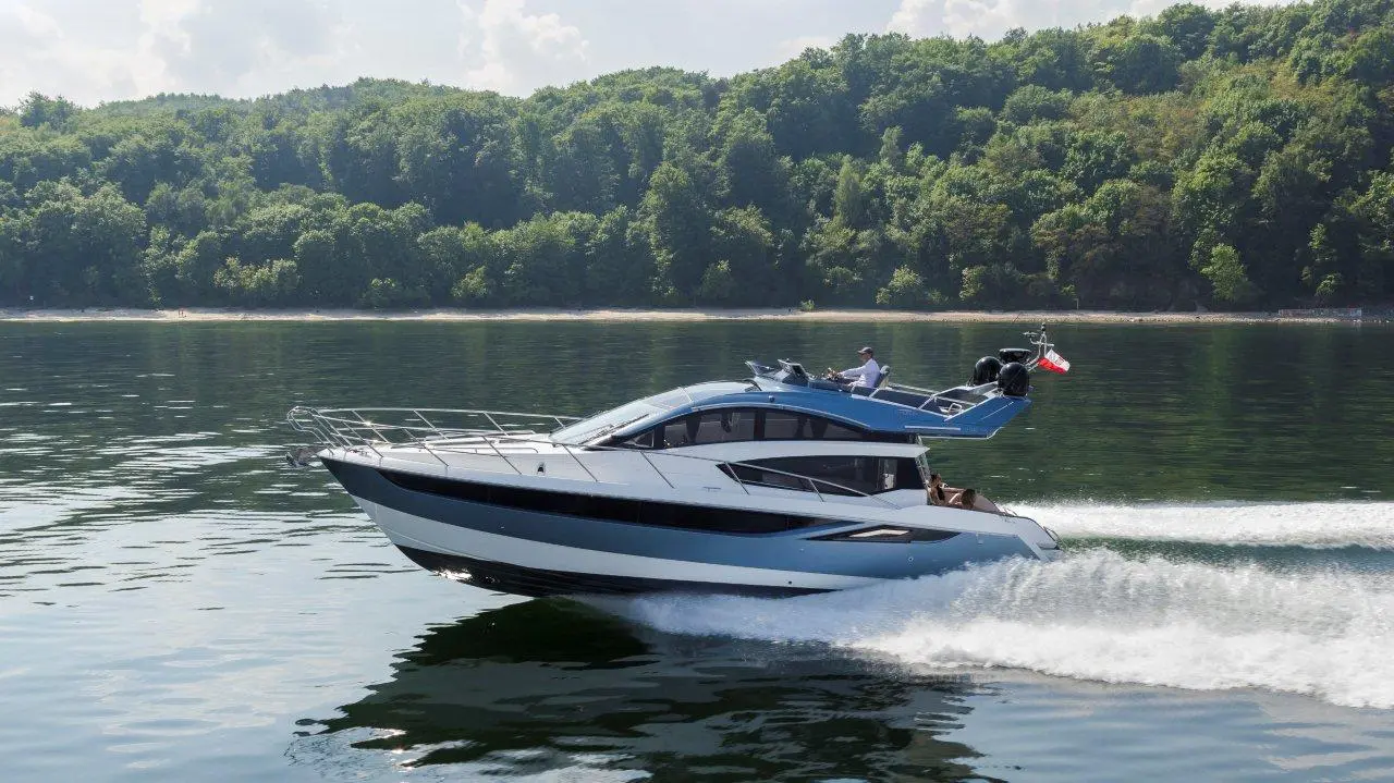 A modern motorboat glides over calm water, with green forests in the background and a passenger at the helm.