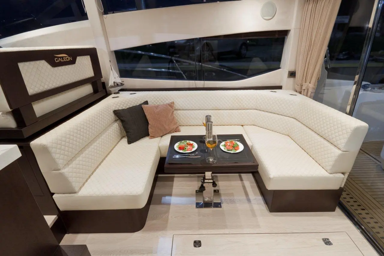 Luxurious yacht interior featuring a white seating area, dark wood table, and plates of salad on a polished surface.