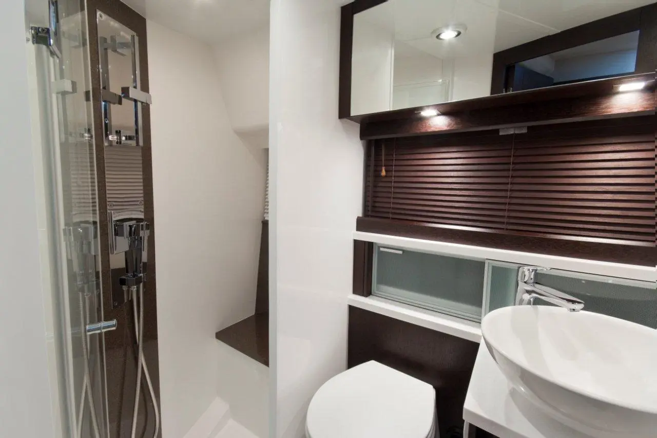 Modern bathroom featuring a glass shower, white toilet, and a round sink with a sleek countertop and wooden blinds.