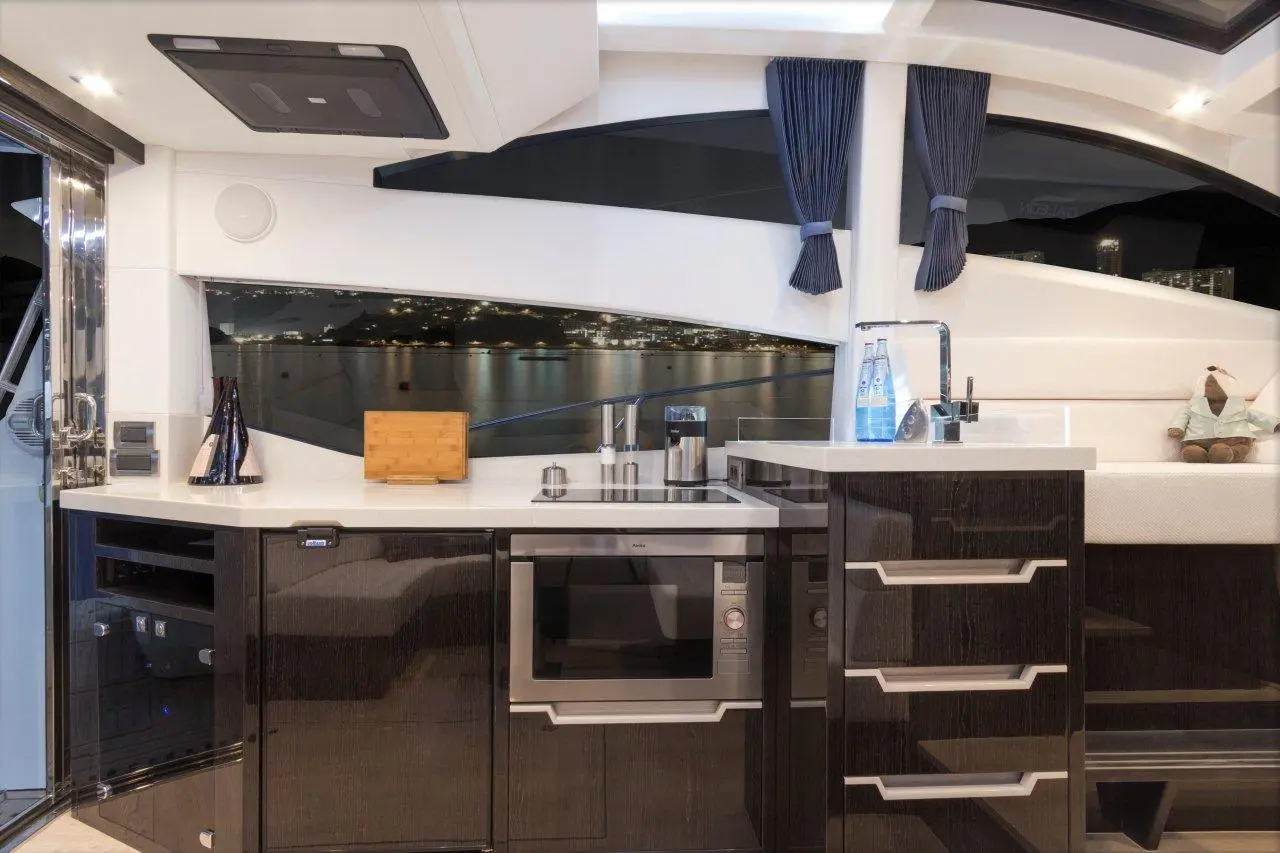 Modern boat kitchen with sleek black cabinets, microwave, sink, and a view of the water illuminated by city lights.