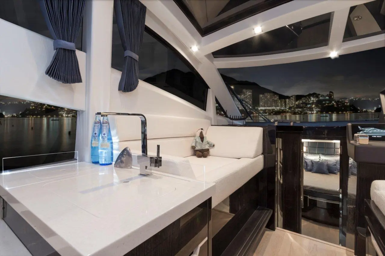Modern yacht interior featuring a stylish lounge, plush seating, countertop, glass windows, and night cityscape view.