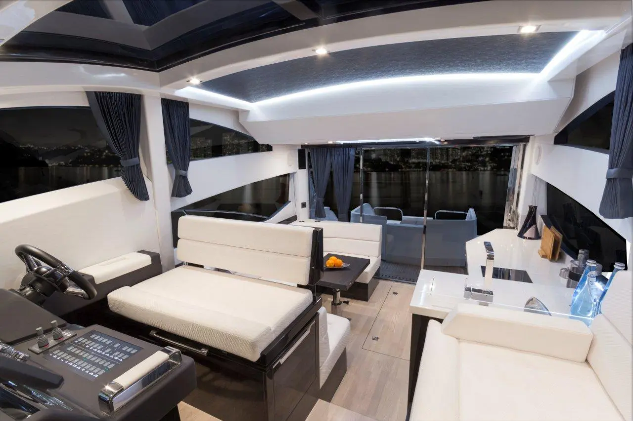 Luxurious yacht interior with a modern steering console, plush seating, and large windows overlooking the night skyline.
